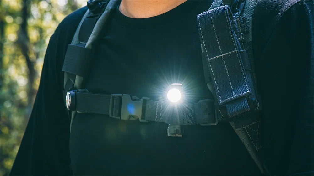 Person wearing a chest harness with a light on, outdoors.