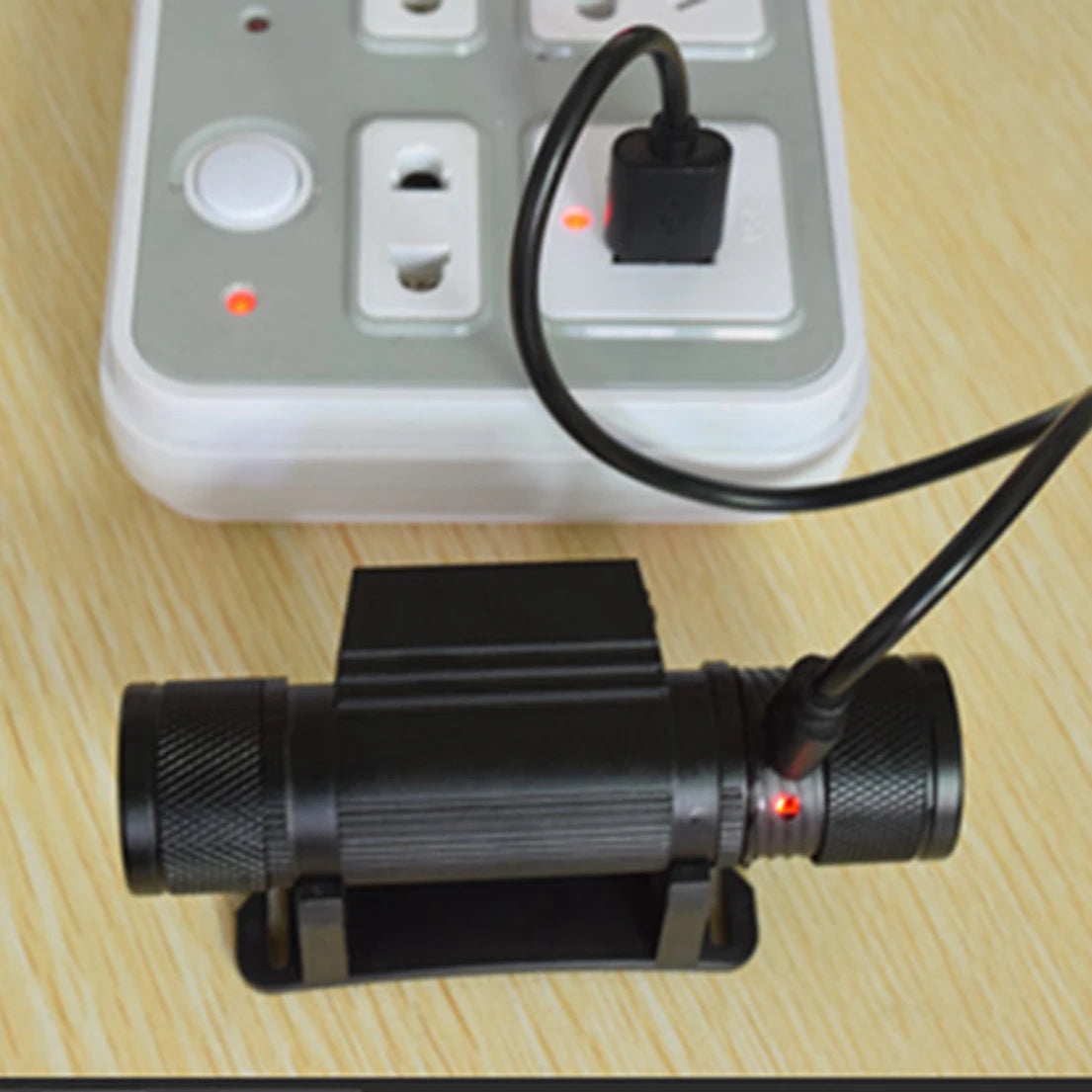 Black flashlight with power adapter connected to a power strip on a wooden surface