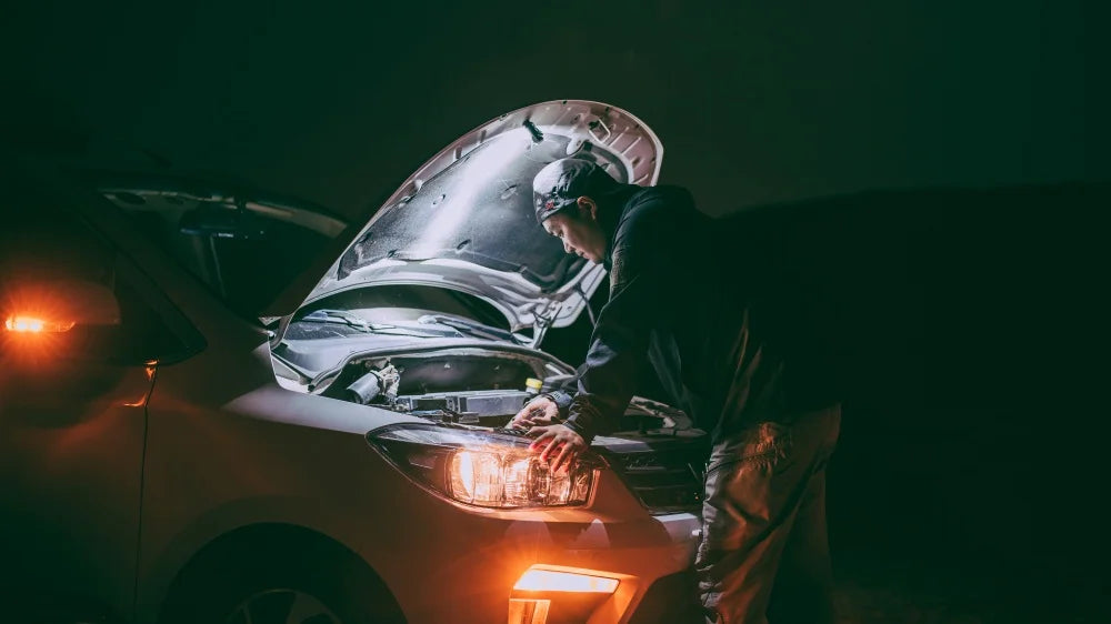 Person working on a car with the hood open at night.