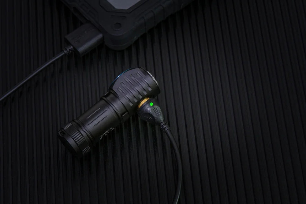Black flashlight with green light on a textured black surface