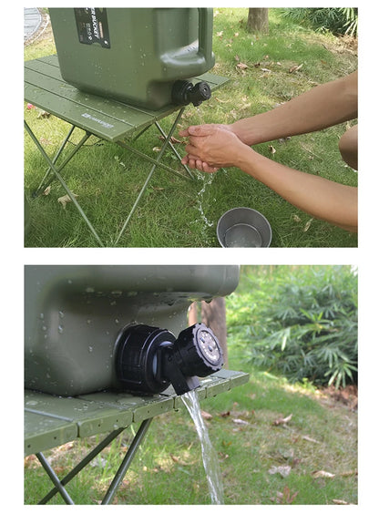 Person washing hands under a green water container on a grassy outdoor setting.