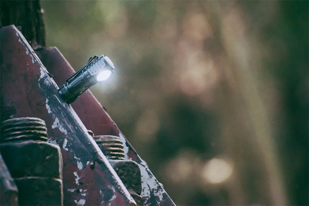 Small flashlight attached to a metal surface with a blurred natural background