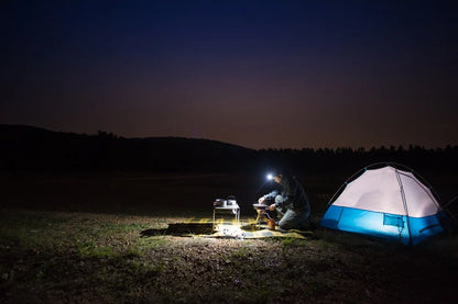 Person camping at night with a tent and lantern in a field