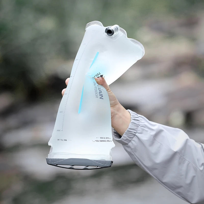 A translucent white collapsible water bottle being held by a hand, with a blurred outdoor background.