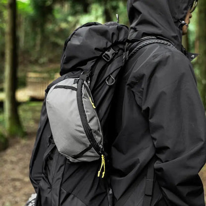 Person wearing a black jacket and backpack with a gray pack in a forest setting