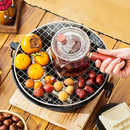 Tea being poured into a glass pot on a small grill with fruits on a wooden table.