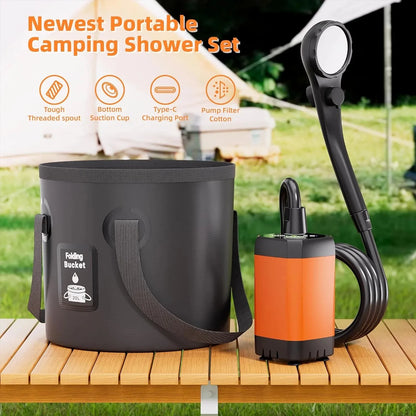 Portable camping shower set displayed on a wooden table with a blurred outdoor campsite background. The set includes a black collapsible bucket, an orange and black portable pump, a black hose, and a handheld shower head.