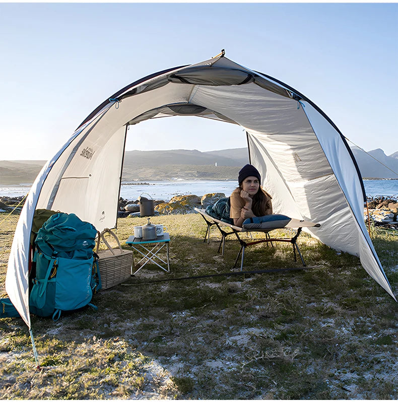 Person sitting inside a large white tent by a body of water with mountains in the background