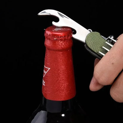 A close-up of a hand using a silver bottle opener tool with a green textured handle to remove a red bottle cap against a black background.