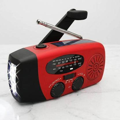 A red and black portable emergency radio with a folding antenna, built-in flashlight, and a small solar panel on top, shown on a light marble surface.