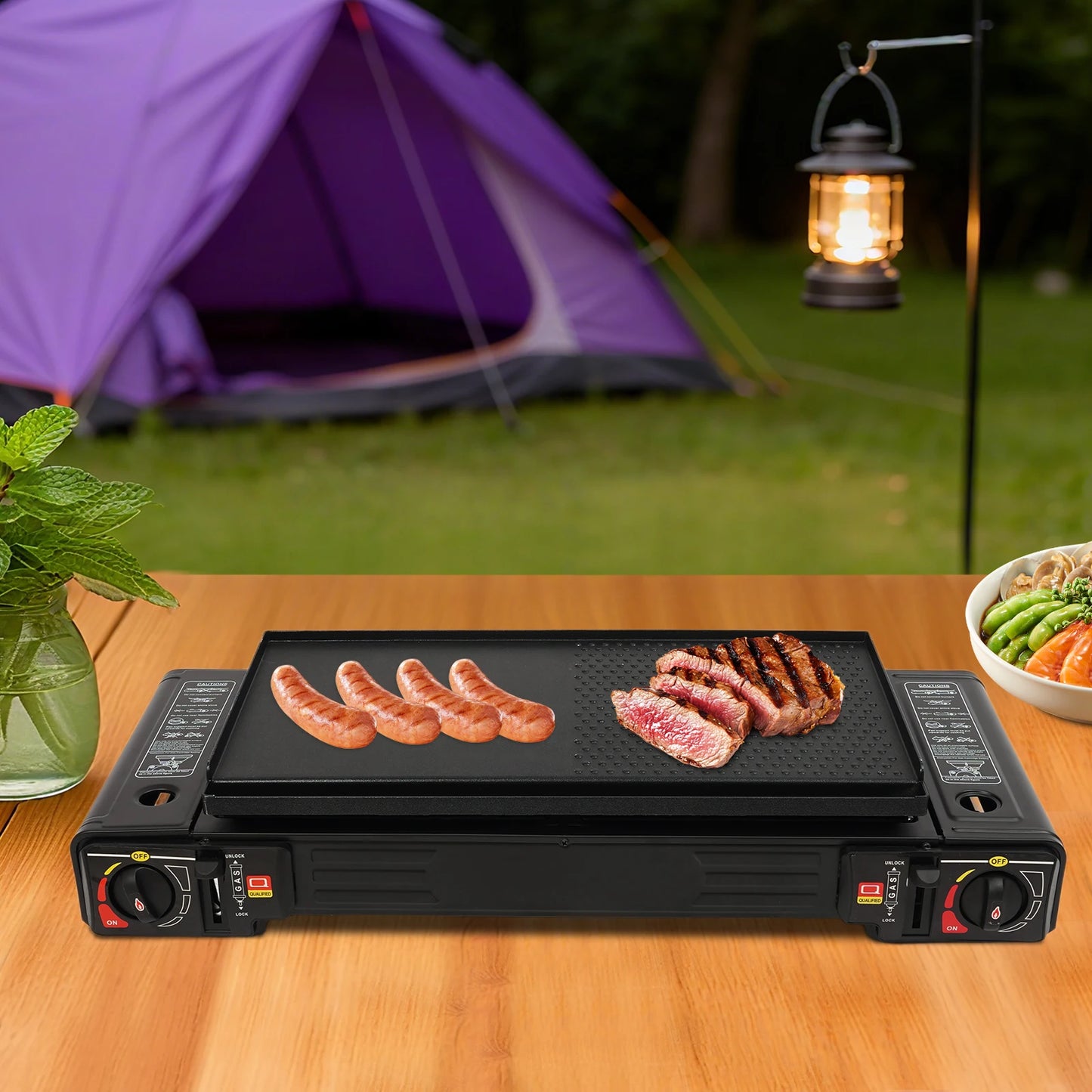 Portable grill with sausages and steak on a camping setup with a tent and lantern in the background.