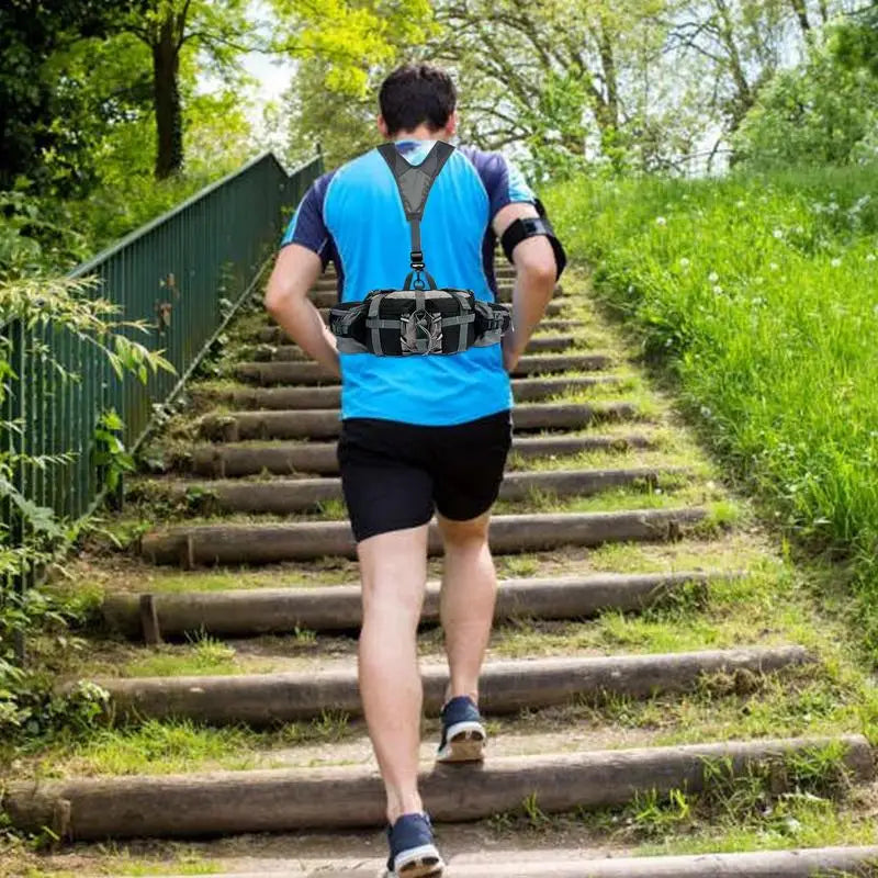 A man running up a grassy wooden staircase outdoors, viewed from behind. He is wearing a bright blue athletic vest, a black waist pack, black shorts, and running shoes.