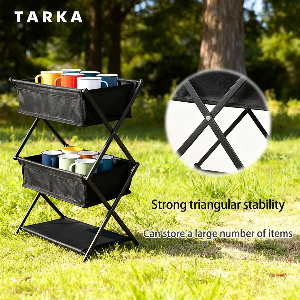 A black metal and fabric outdoor storage cart with two tiers and a lower shelf, shown on grass with trees in the background. The cart holds colorful mugs, and text on the image highlights strong triangular stability and storage capacity.