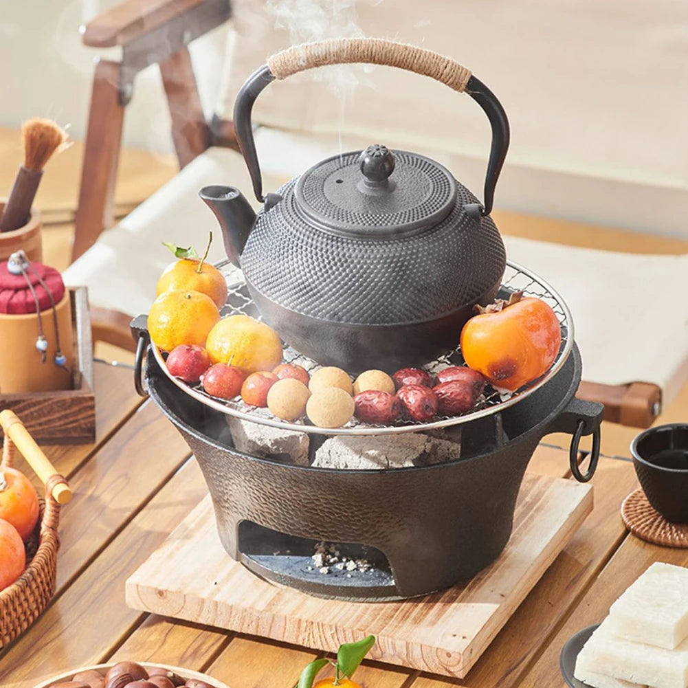 Black cast iron teapot on a small stove with fruits on a wooden table