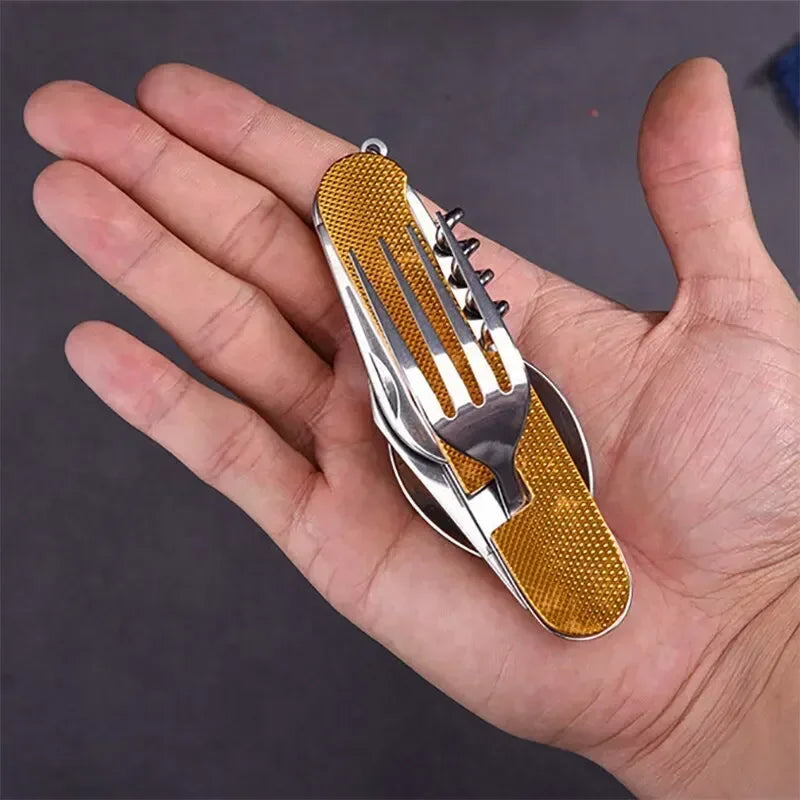 A stainless steel folding utensil with a textured gold handle, shown folded and held in a person's hand against a dark gray background.