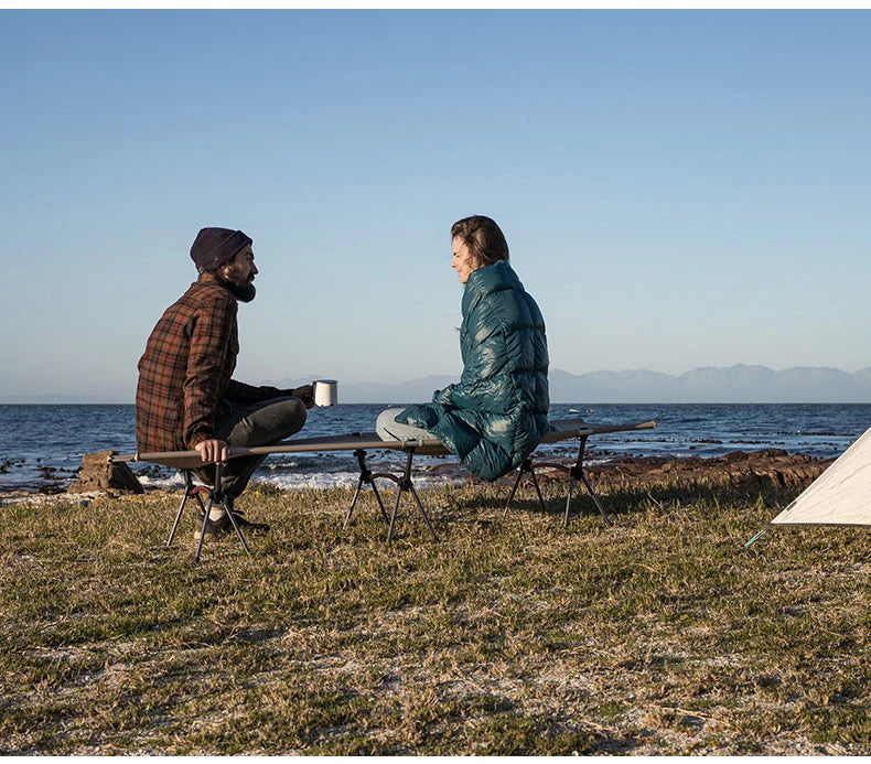 Two people sitting on a bench by the ocean with mountains in the background.