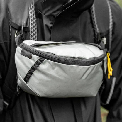Gray waist bag attached to a backpack with a person wearing it outdoors.