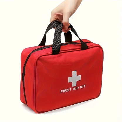 A red first aid kit bag with black handles, held by a hand against a plain white background. The bag features a white cross and the text 'FIRST AID KIT' printed on the front.