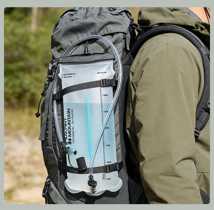 A close-up of a hiking backpack with a clear water bottle reservoir attached, worn by a person in an outdoor forest setting. The reservoir has black straps, a blue-tinted tube, and visible branding that reads 'MOUNTAIN AIR'.