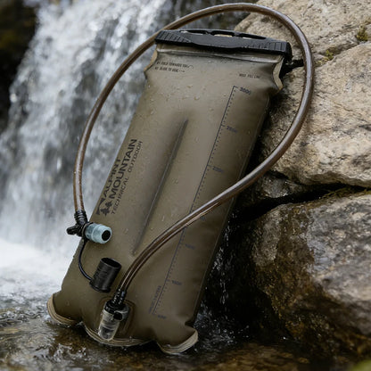 An olive drab green Accu-Mountain hydration bladder with attached drinking tubes, resting against large rocks next to a flowing waterfall.