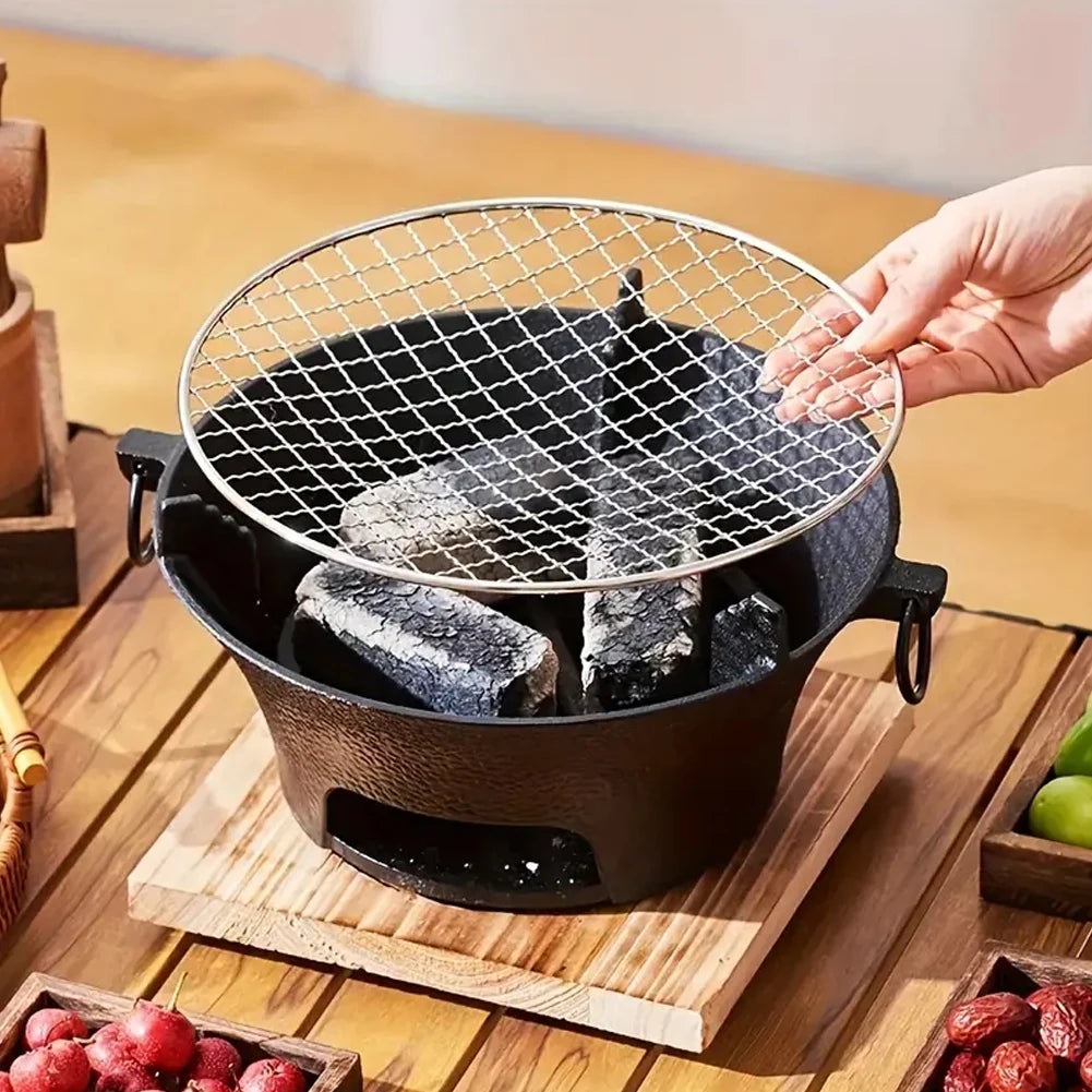 Small grill with charcoal on a wooden surface, surrounded by fruits and vegetables.