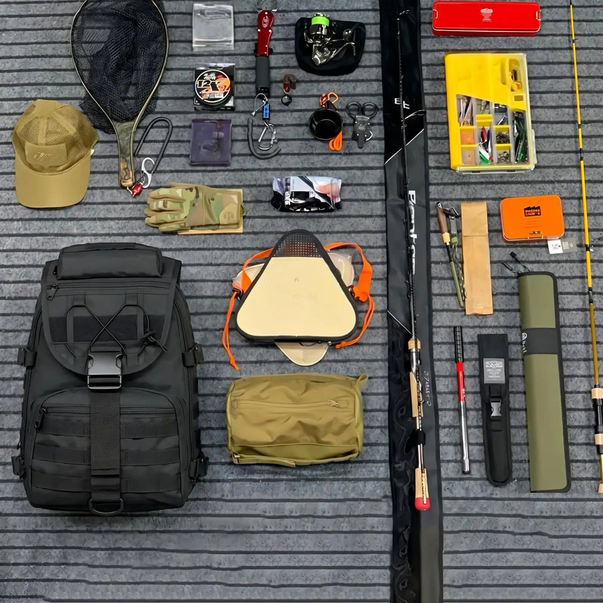 A flat-lay arrangement of fishing gear and accessories on a gray ribbed mat, including a black backpack, fishing rods, a yellow tackle box, a tan cap, gloves, a net, a paddle, hooks, line, and other fishing supplies.