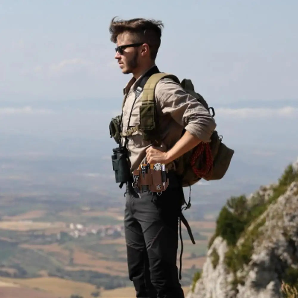 Man with a backpack and tactical gear standing on a mountain with a scenic view.