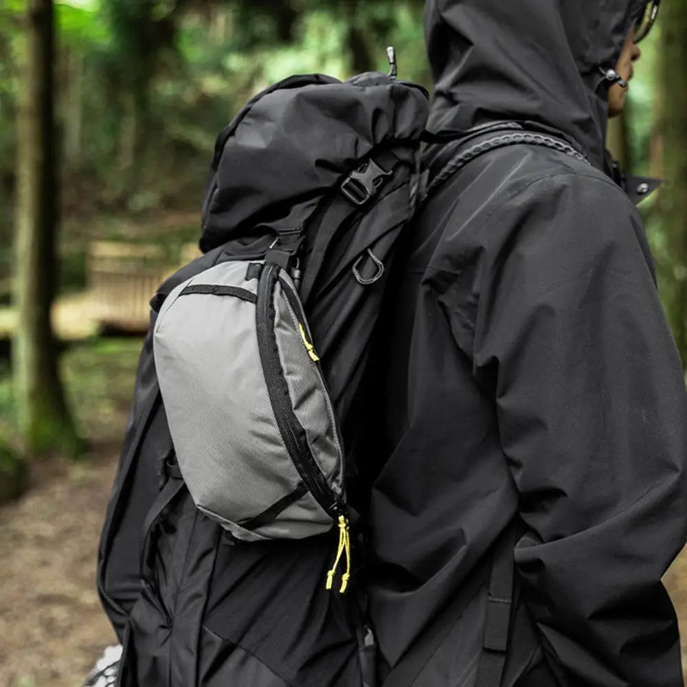Person wearing a black jacket and backpack with a gray pack in a forest setting