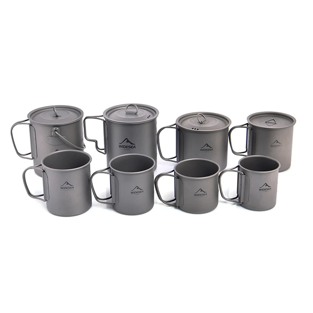 A set of eight gray titanium camping cookware pieces, including mugs, cups, and pots with lids, arranged on a plain white background. Each piece features a small white printed mountain logo with the brand name 'WODGA' in the center.