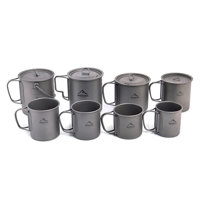 A set of eight gray titanium camping cookware pieces, including mugs, cups, and pots with lids, arranged on a plain white background. Each piece features a small white printed mountain logo with the brand name 'WODGA' in the center.