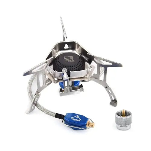 A portable titanium camping stove with a blue and gold fuel regulator hose, shown with its metal fuel canister on a white background.