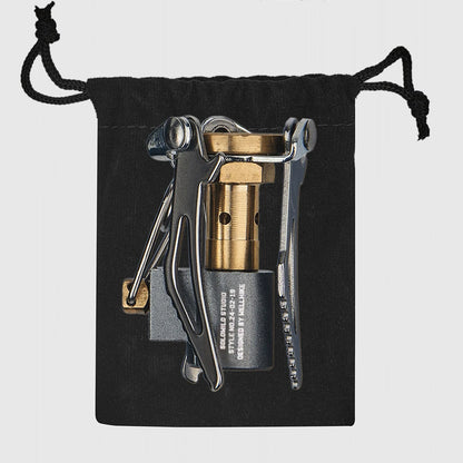 Multitool with brass component and knife on a black drawstring pouch against a light gray background