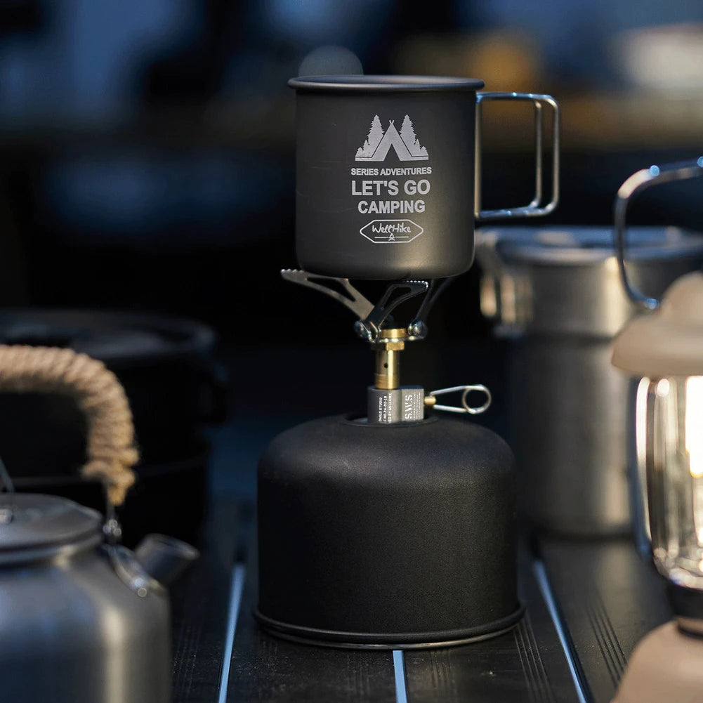 Black camping mug with 'Let's Go Camping' text on a stove, surrounded by camping gear.